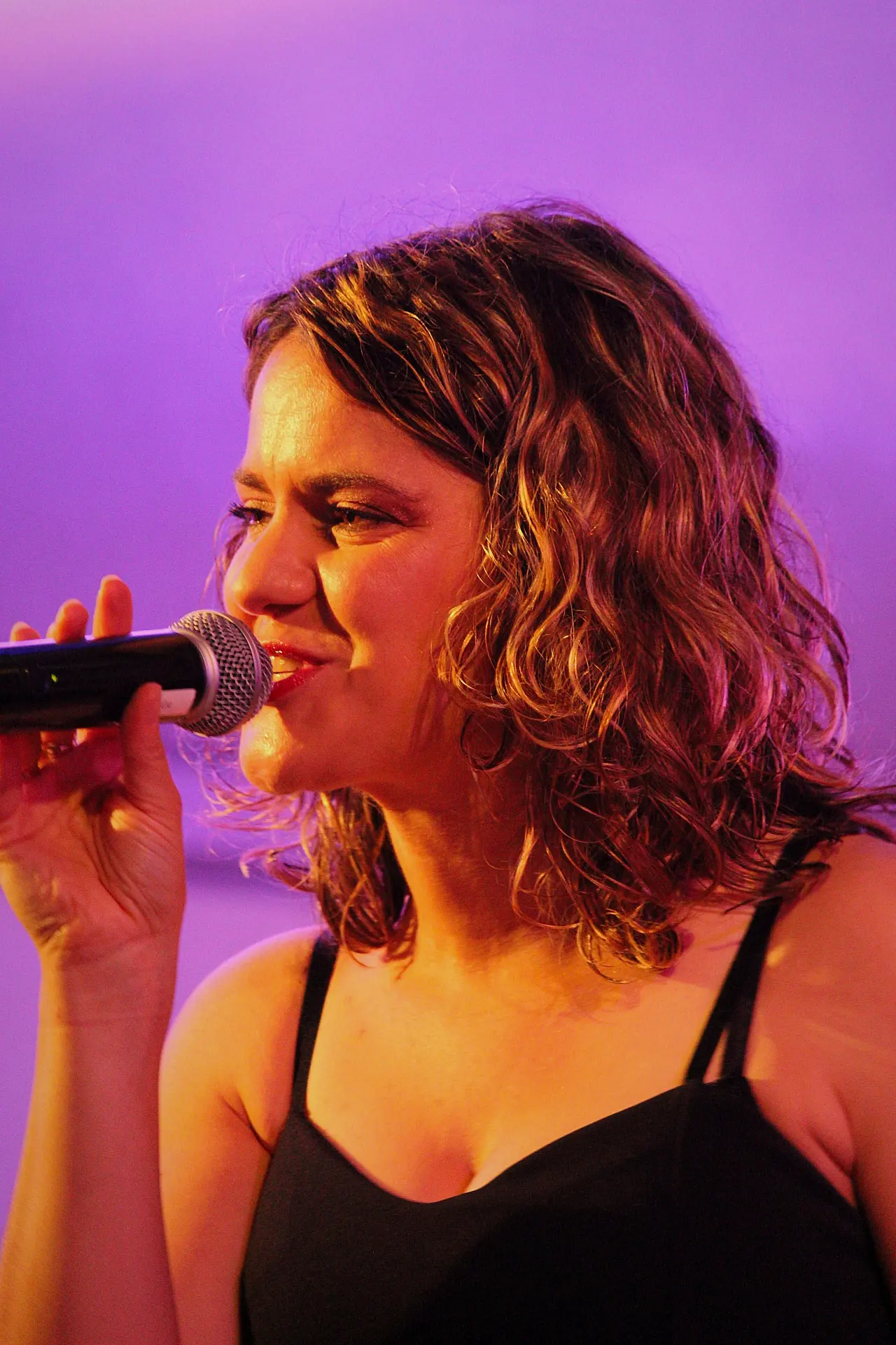 Chanteuse du groupe Watts Up au micro sous une lumière rose, en concert, par Léa Créon Bossonnet